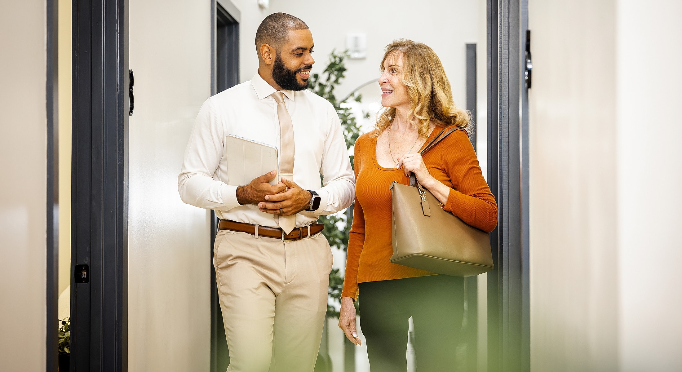 Two professionals smiling and conversing in hallway.